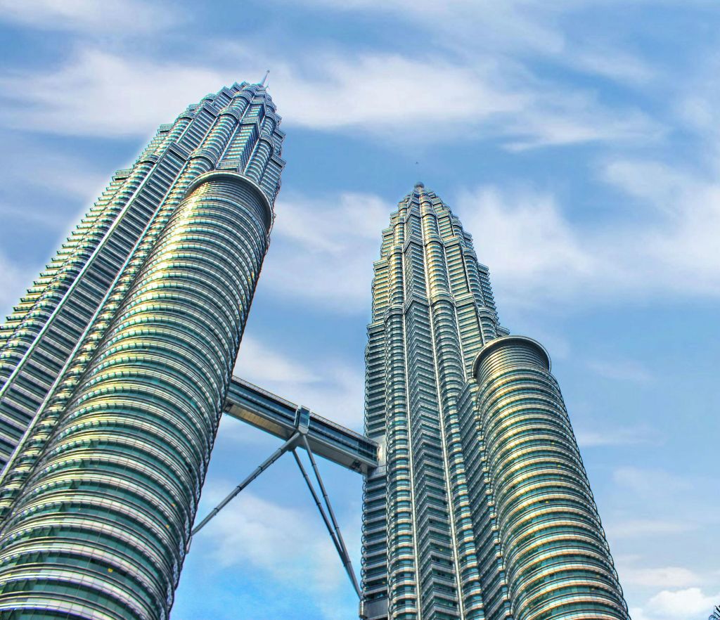 푸른 하늘과 흩어져 있는 구름을 배경으로 스카이 브리지로 연결된 두 개의 현대적인 고층 건물.