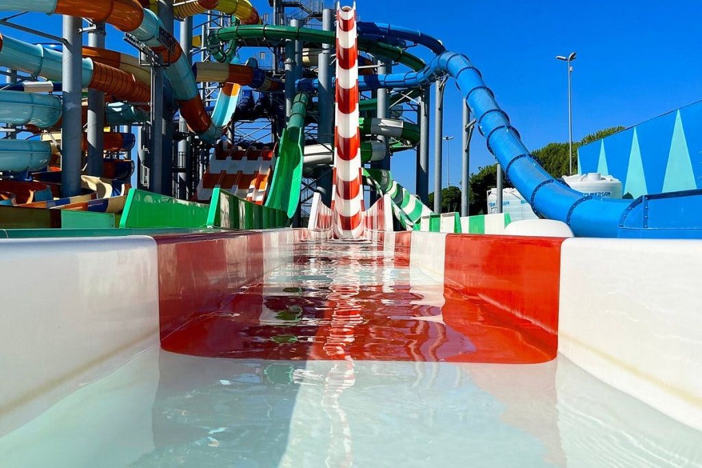 빨간색과 흰색 줄무늬가 있는 다채로운 워터파크 슬라이드는 다른 슬라이드와 구조물로 둘러싸인 얕은 물로 이어집니다.