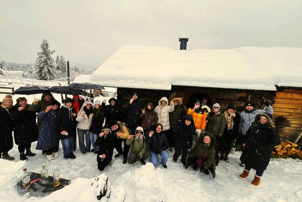 눈 덮인 나무 오두막에서 겨울 옷을 입은 한 무리의 사람들이 눈 덮인 풍경 속에서 포즈를 취하고 있습니다.