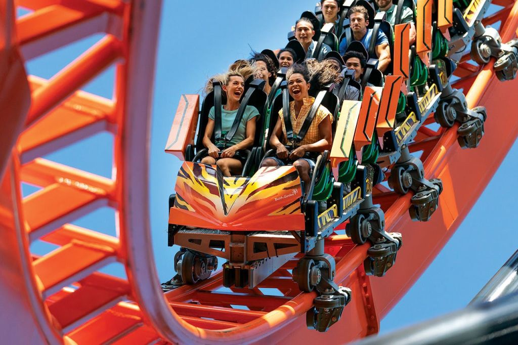 화창한 날에 오렌지색 롤러코스터를 타고 내려오며 즐거운 비명을 지르는 사람들.