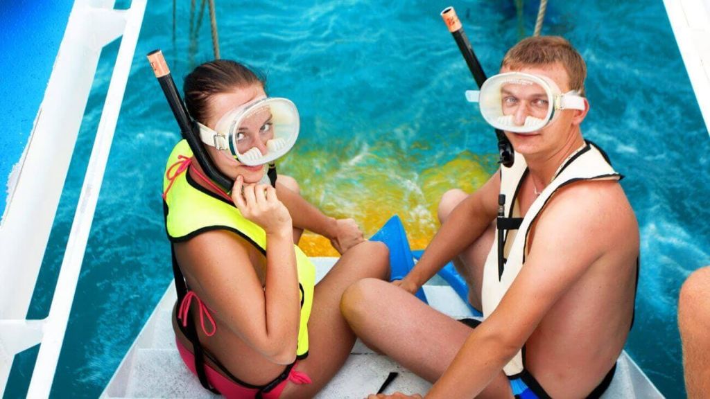 스노클링 마스크와 구명조끼를 착용한 남성이 보트에 앉아 스노클링을 즐길 준비를 하고 있습니다. 푸른 물과 다른 사람의 일부가 보입니다.