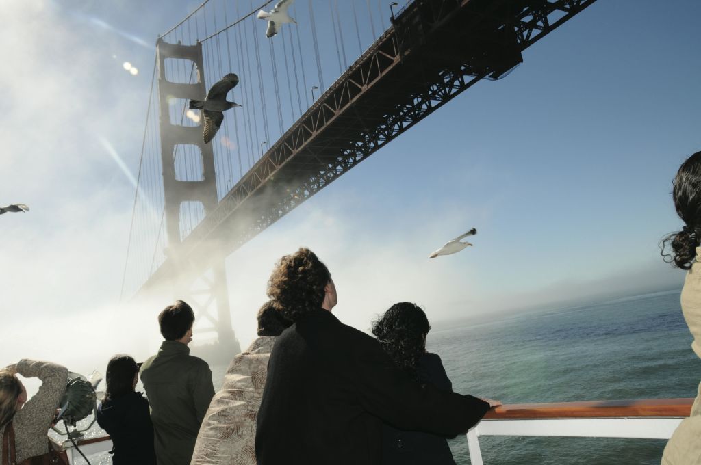 보트 갑판에 올라 금문교를 바라보고 있는 사람들로, 갈매기가 물 위로 날아다니고 안개가 자욱한 하늘이 펼쳐집니다.