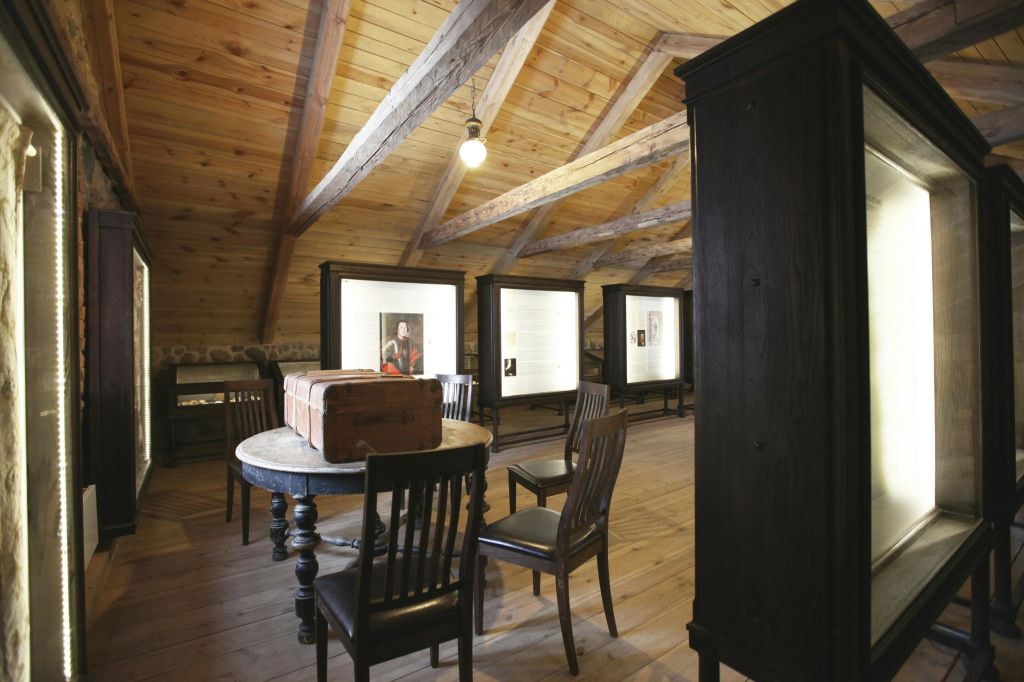 나무 대들보가 놓인 다락방, 벽에 진열된 다락방, 원형 테이블, 나무 의자, 테이블 위에 놓인 빈티지 여행 가방.