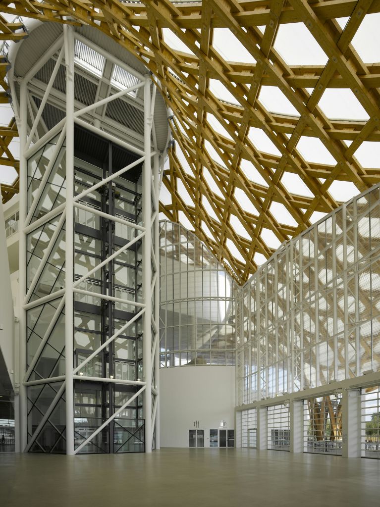 유리 엘리베이터, 커다란 유리 벽, 나무 격자 천장이 있는 현대적인 건물의 내부.