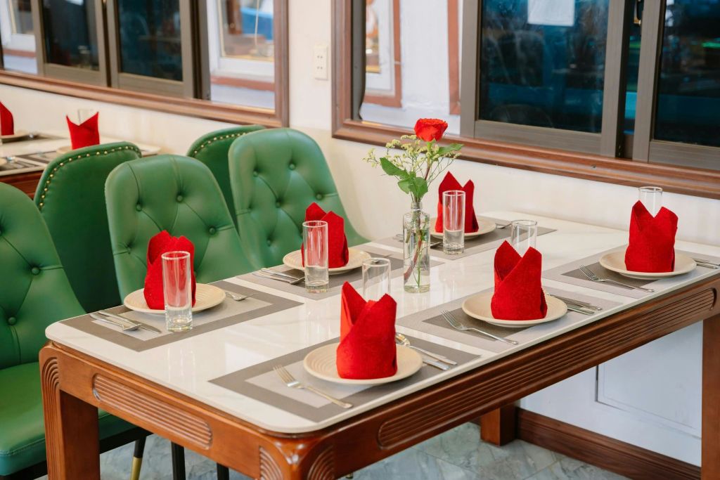 빨간 냅킨, 투명한 음료수 잔, 빨간 장미와 하얀 꽃이 한 송이 놓인 꽃병이 놓인 6인용 식탁입니다.