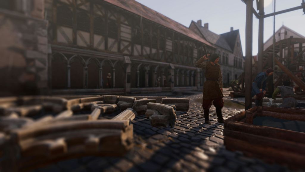 한 사람이 나무 기둥과 아치가 있는 중세 건물 앞, 흩어져 있는 돌 블록 근처의 자갈길에 서 있습니다.