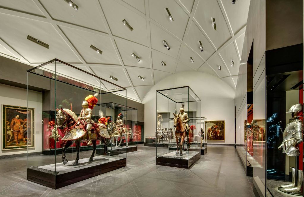 아치형의 기하학적 천장 아래 유리 케이스에 장식된 말의 갑옷이 특징인 박물관 전시품.