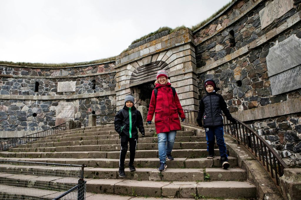 따뜻한 옷을 입은 세 사람이 오래된 석조 요새 앞에서 돌계단을 걸어가고 있습니다.