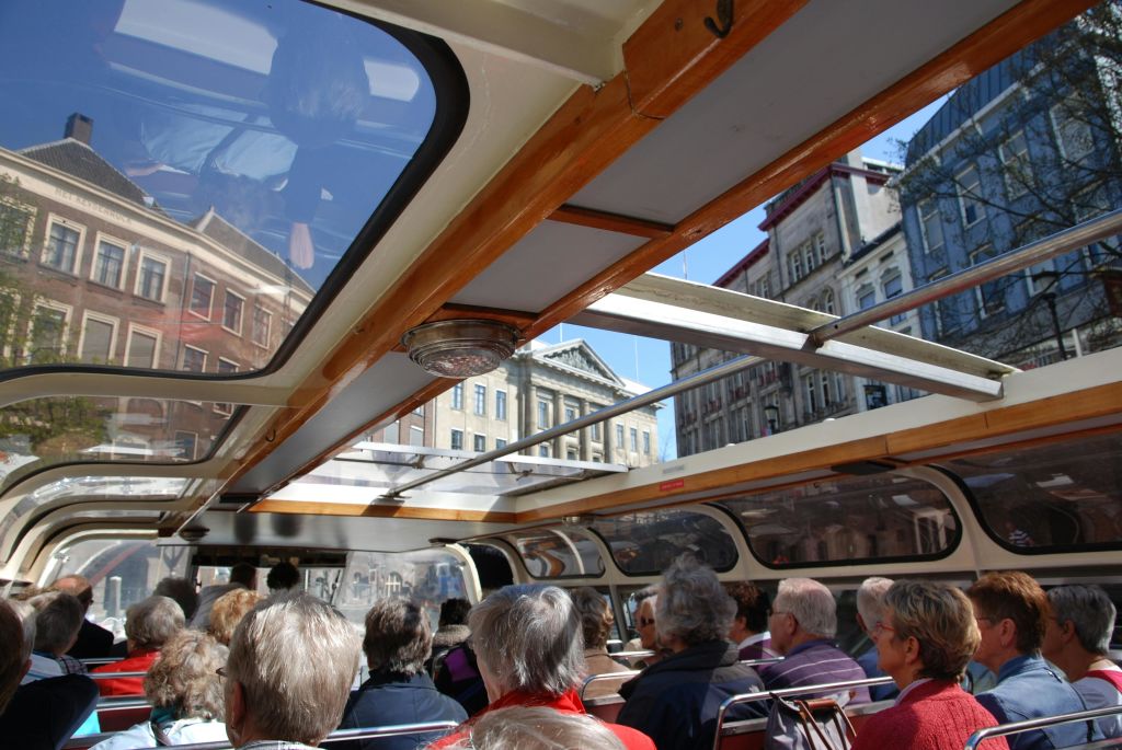 한 무리의 사람들이 오픈탑 버스에 앉아 화창한 날 유서 깊은 건물을 바라보고 있습니다.