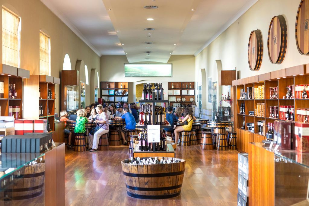 나무 바닥, 병 선반, 아치형 창문이 있는 밝은 조명의 방에서 사람들이 통으로 만든 테이블에 앉아 있습니다.