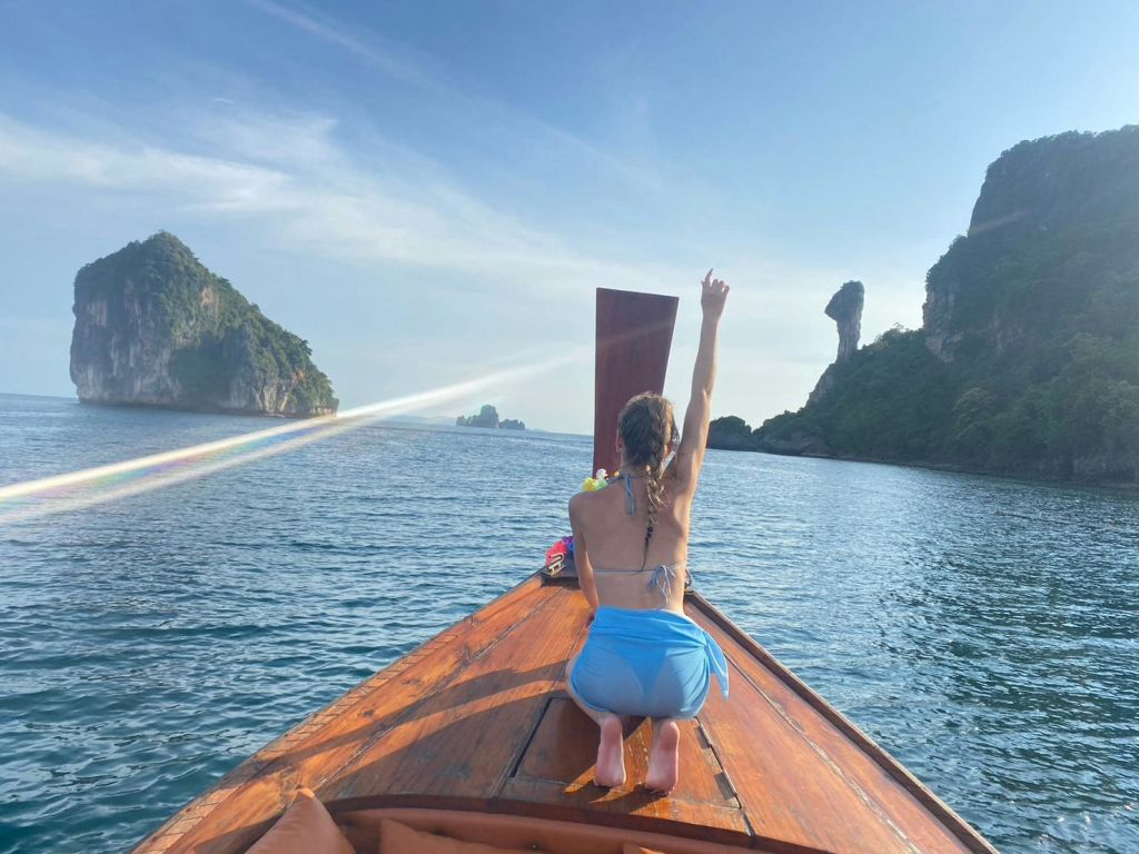 나무 보트에 무릎을 꿇고 맑고 푸른 바다와 화창한 하늘 아래 먼 바위 섬을 향해 팔을 드는 사람.