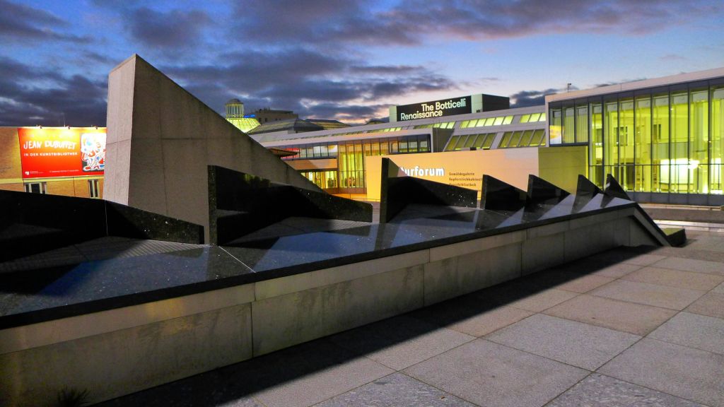 날카로운 각도와 어두운 반사 표면을 가진 현대적인 건물로, "보티첼리 르네상스" 전시회 표지판이 있습니다.