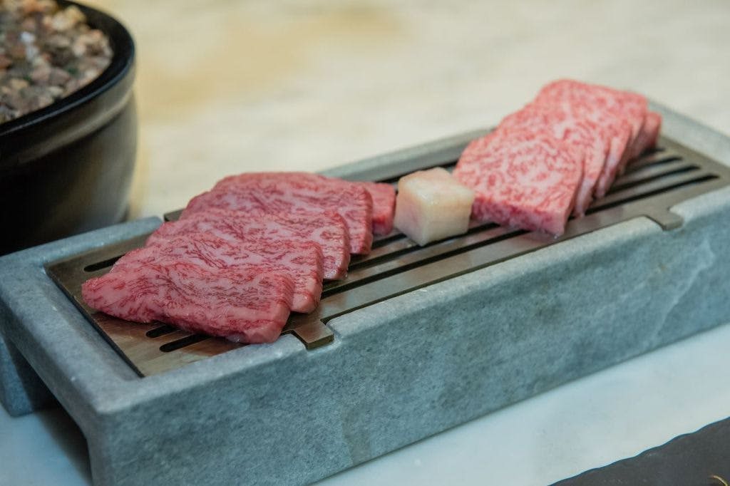 직사각형 석재 받침대 위에 구운 구슬 생고기와 금속 그릴에 놓인 지방 조각.