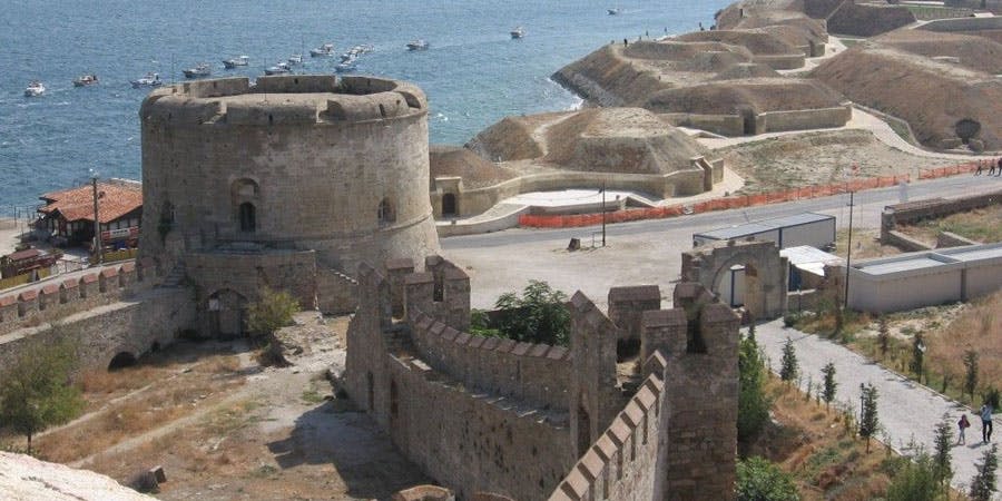 바다에 여러 척의 보트가 있는 해안선이 내려다보이는 석조 요새로 둥근 탑과 신축성 있는 벽이 있습니다.
