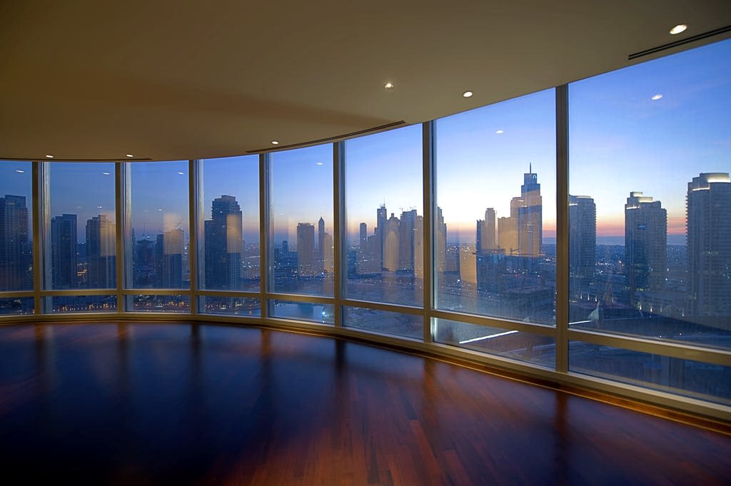 석양에 도시 스카이라인의 전경을 감상할 수 있는 바닥에서 천장까지 이어지는 창문이 있는 넓은 객실입니다.