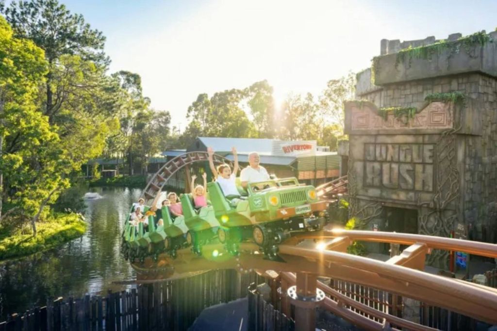 녹색 지프를 형상화한 롤러코스터가 녹음으로 둘러싸인 채 승객들이 팔을 들고 트랙을 따라 이동합니다.