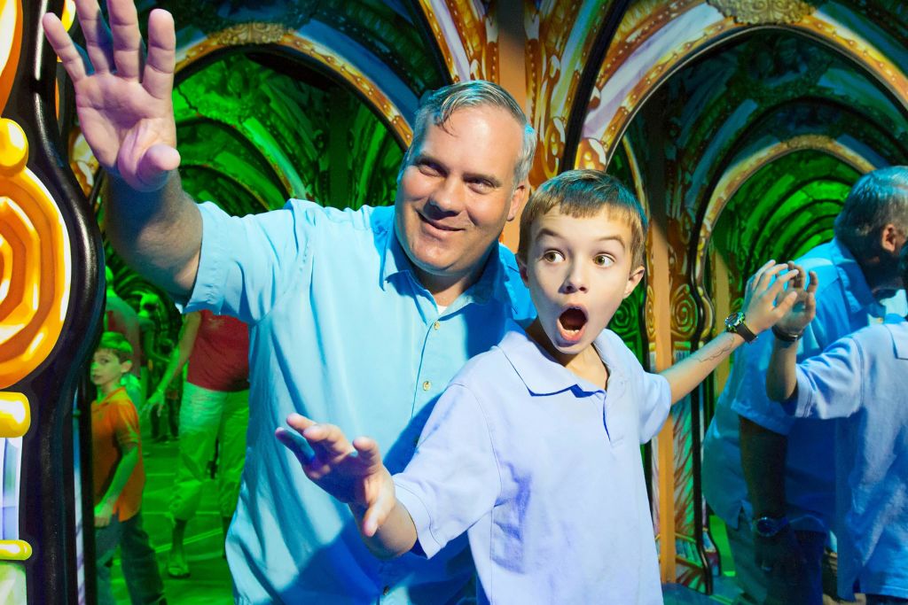 한 남자와 어린이가 화려하고 반사된 펀하우스에서 놀라움과 흥분으로 반응합니다.