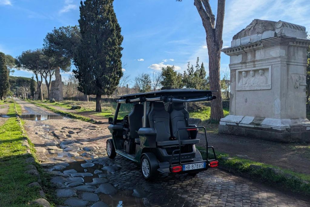 대낮에 나무와 유서 깊은 석조 건물로 둘러싸인 자갈길에 주차된 소형 전기 차량.