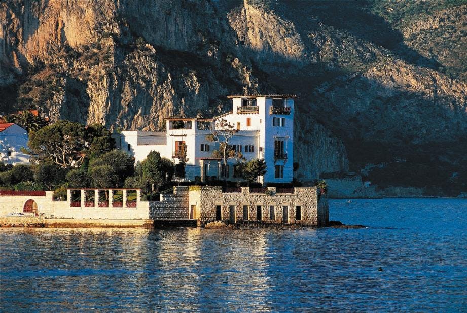 바위 언덕을 배경으로 물이 내려다보이는 여러 개의 발코니와 테라스가 있는 흰색 건물입니다.