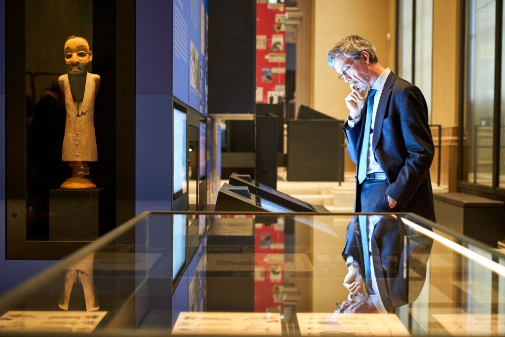 반사 유리를 통해 볼 수 있는 박물관 전시물에 고대 조각상과 정보 플래카드가 있는 디스플레이 케이스.