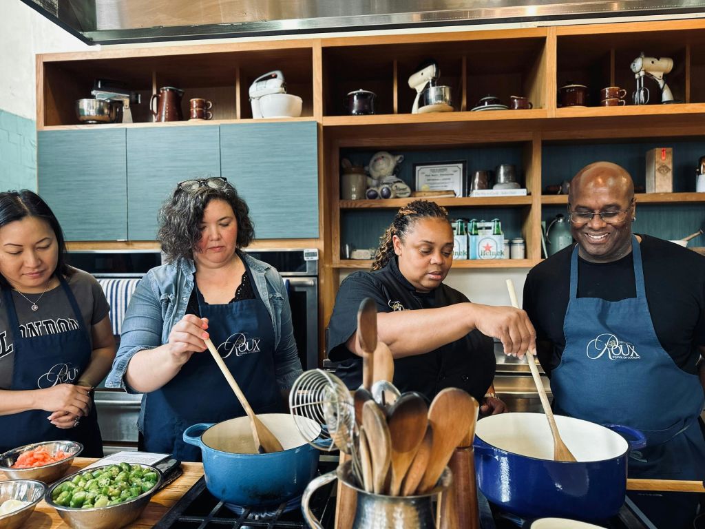 주방에서 세 사람이 앞치마를 두르고 다양한 재료와 식기를 조망할 수 있습니다.