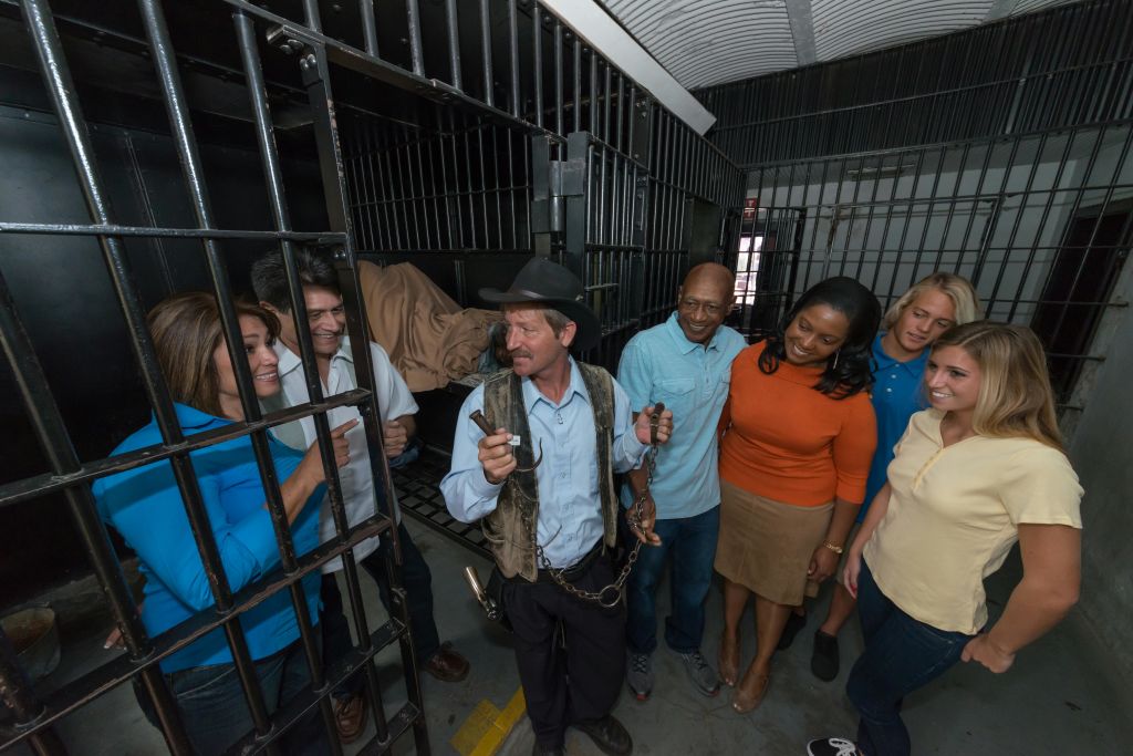 수갑을 찬 남성이 감방 옆에 서서 감방 안팎에서 웃고 있는 사람들과 이야기를 나누고 있습니다.