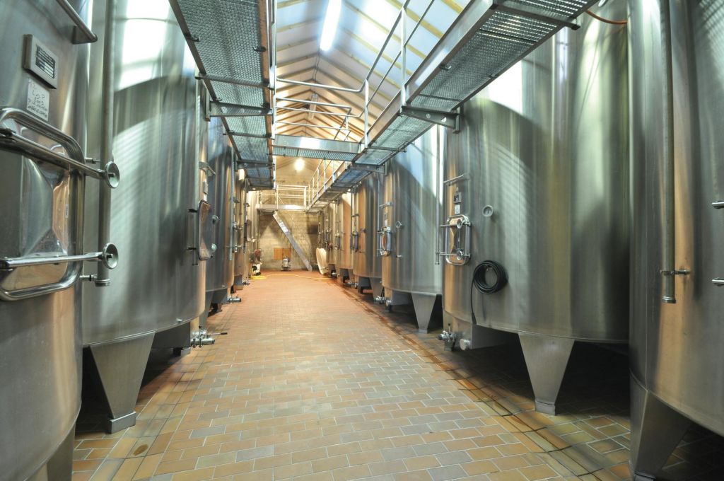 여러 개의 스테인리스 스틸 탱크와 천장 조명으로 비춰지는 오버헤드 통로가 있는 대형 산업실입니다.