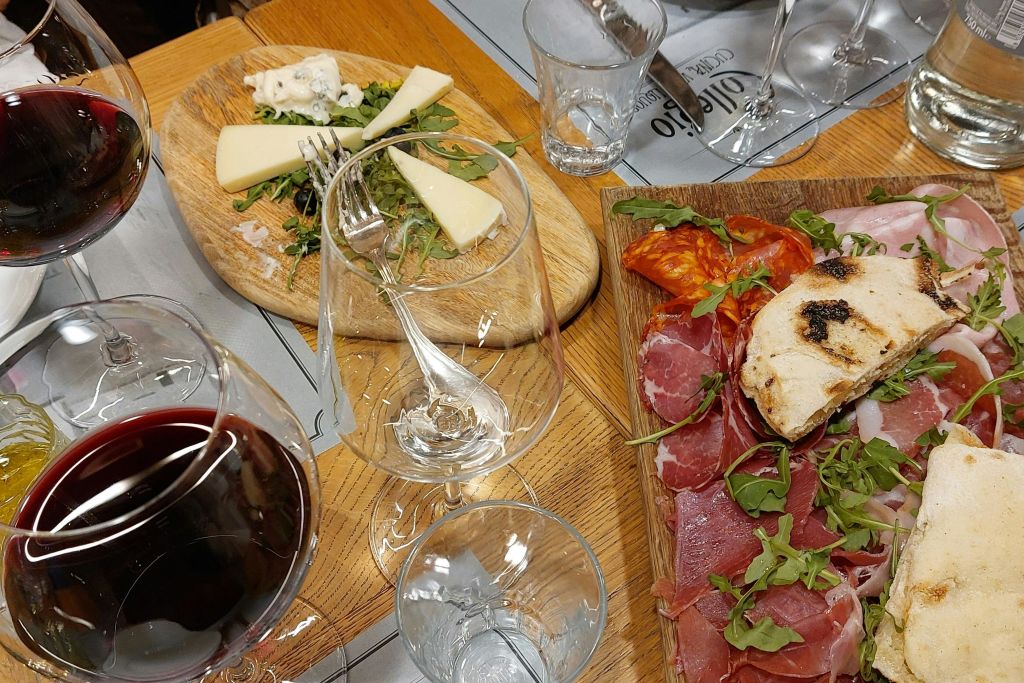 나무 테이블 위에 고기, 치즈, 아루굴라, 레드 와인 한 잔이 놓인 샤퀴트리 보드.