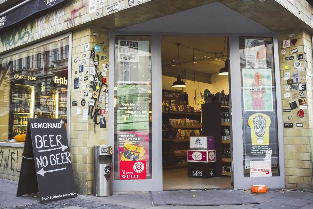 제품 내부 선반이 있는 열린 유리문과 쓰레기통 옆 스티커로 덮인 간판이 있는 매장 입구.