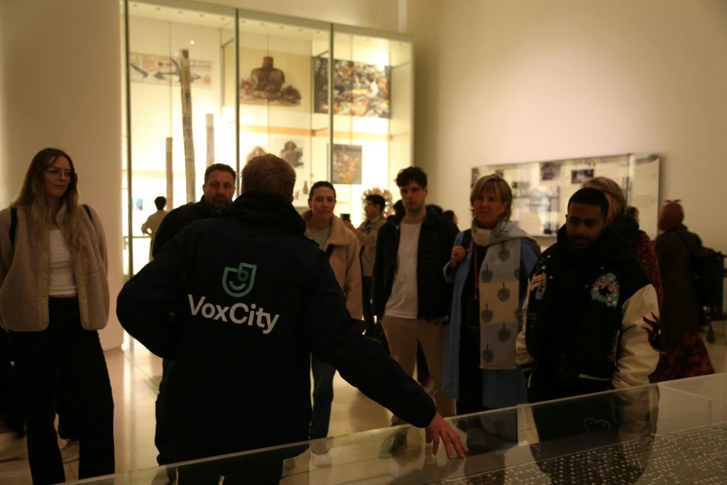 박물관에서 'VoxCity' 재킷을 입은 가이드가 그룹에 전시물을 설명하고 있습니다.