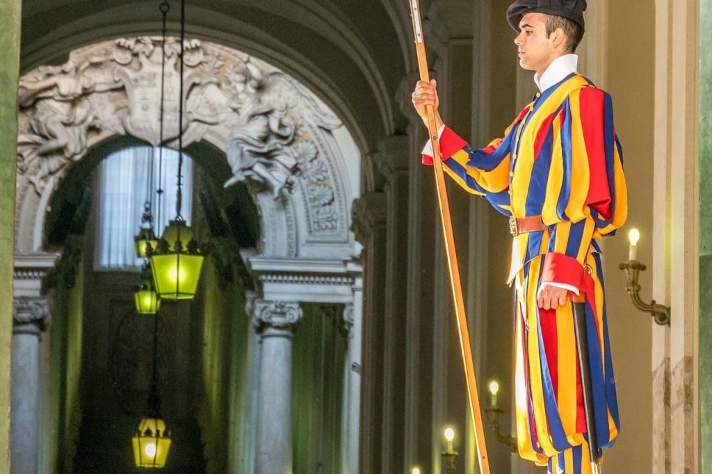 화려한 색상의 줄무늬 유니폼과 모자를 쓴 경비원이 화려한 건물 내부에 긴 기둥을 들고 있습니다.