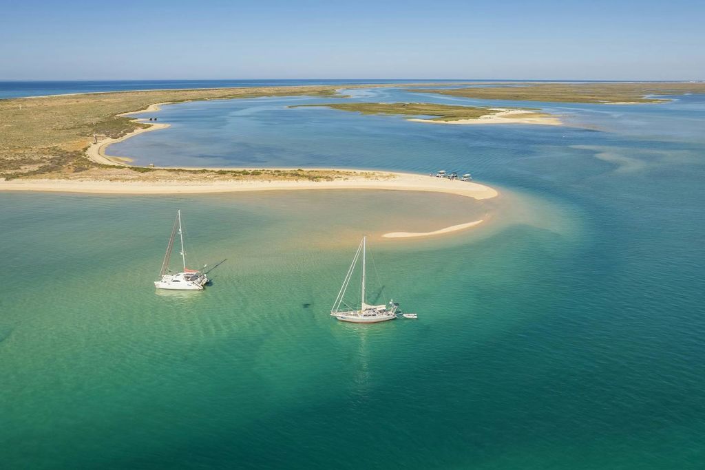 청록색의 맑은 물이 흐르는 사막의 섬 근처에 정박한 요트는 해안 유입구와 차분하고 탁 트인 바다로 둘러싸여 있습니다.