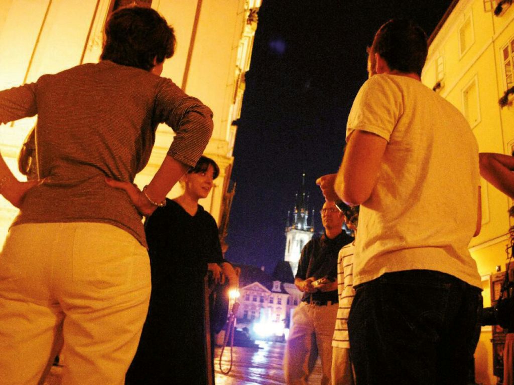 밤에 불이 켜진 건물과 탑을 배경으로 밖에서 이야기를 나누는 사람들의 모임.