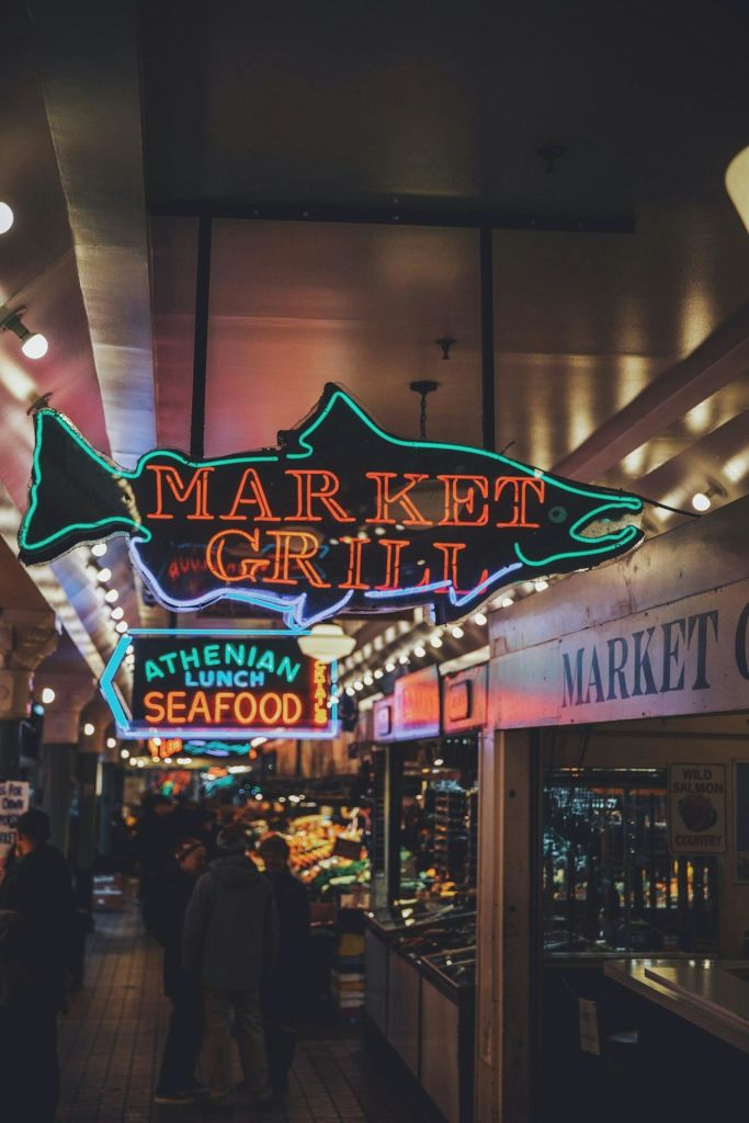 노점을 배경으로 '마켓 그릴' 과 '아테네 점심 해산물' 을 읽는 네온사인이 빛나는 마켓 인테리어.
