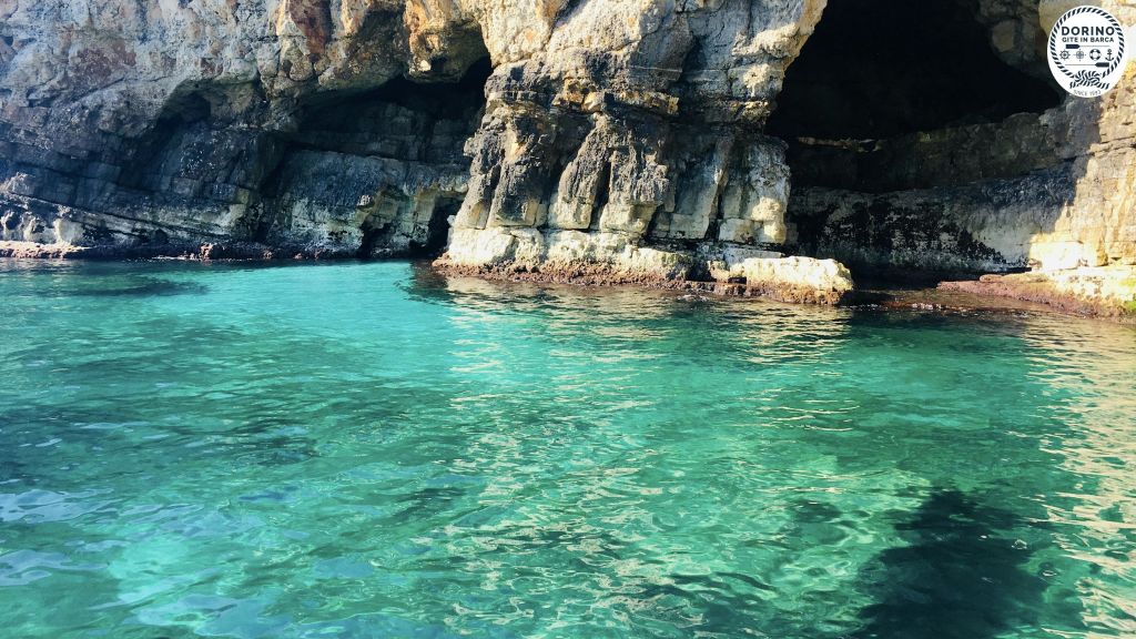 청록색의 맑은 물 위로 어두운 동굴이 펼쳐진 바위 절벽.