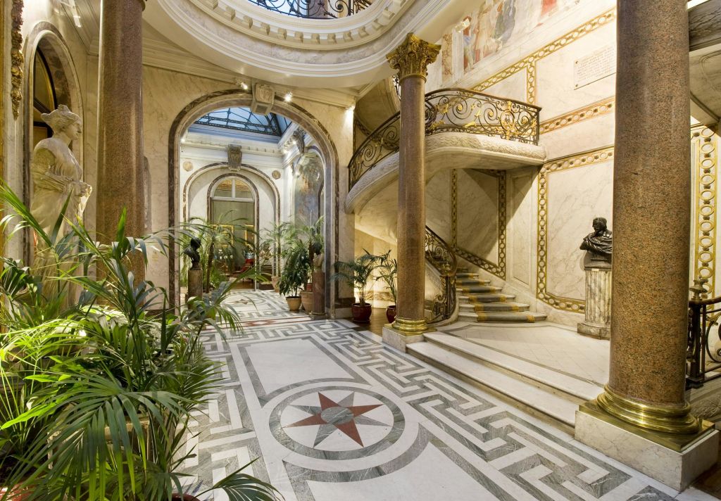조명이 밝은 아트리움에는 대리석 바닥, 화려한 계단, 기둥, 화분, 조각품이 있는 정교한 인테리어가 돋보입니다.
