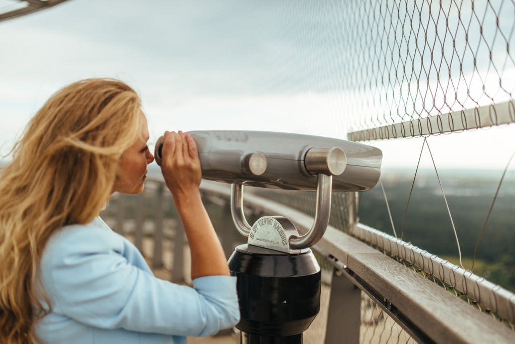 안전 울타리와 흐릿한 풍경을 배경으로 전망대에서 동전으로 움직이는 풍경을 감상하는 사람.