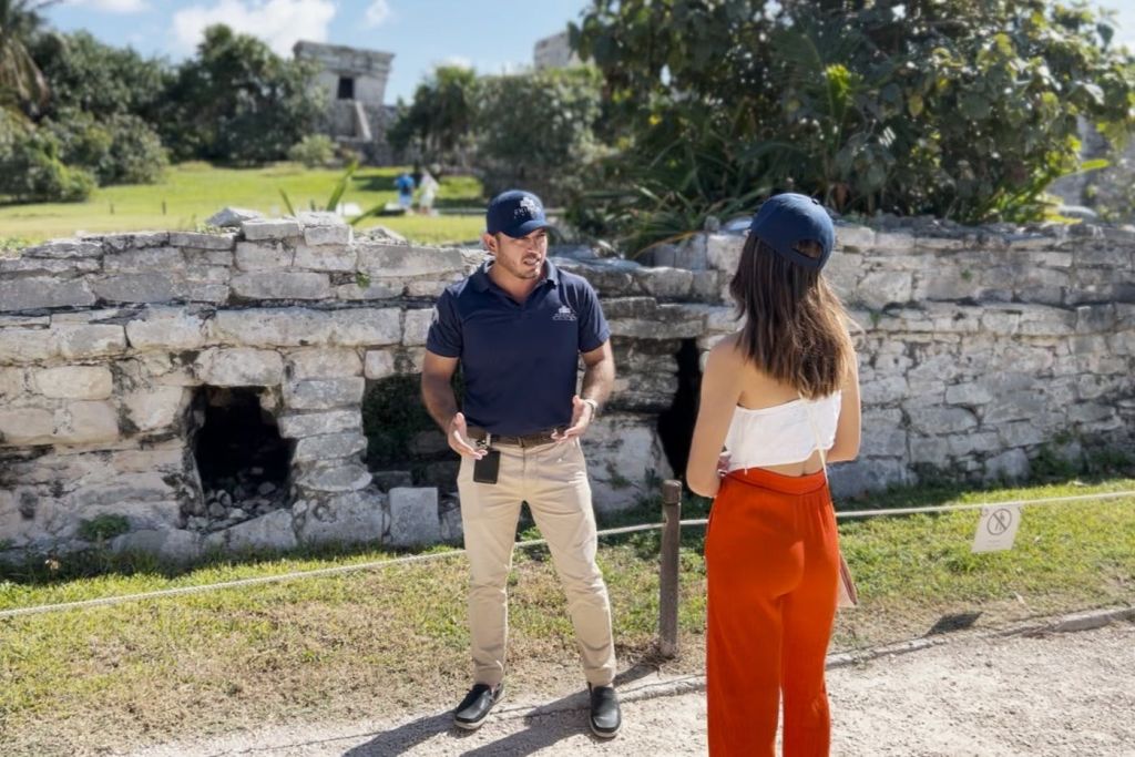 고대 석조 유적 앞에서 여성에게 가이드 투어를 제공하는 평상복을 입은 남성.