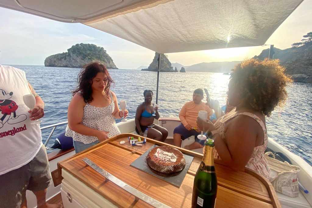테이블 위에 초콜릿 케이크가 놓인 보트에 네 명이 앉아 음료를 마시고 있습니다. 섬이 배경으로 보입니다.