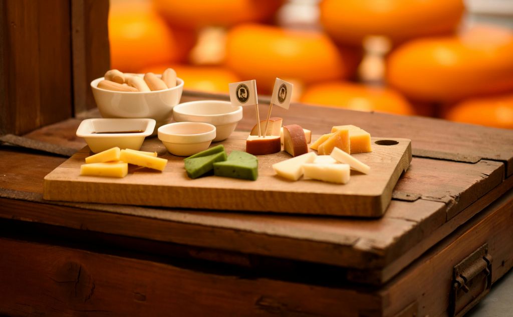 소박한 테이블 위에 작은 흰색 그릇이 놓인 나무 보드에 모듬 치즈와 크래커, 배경에 흐릿한 오렌지.