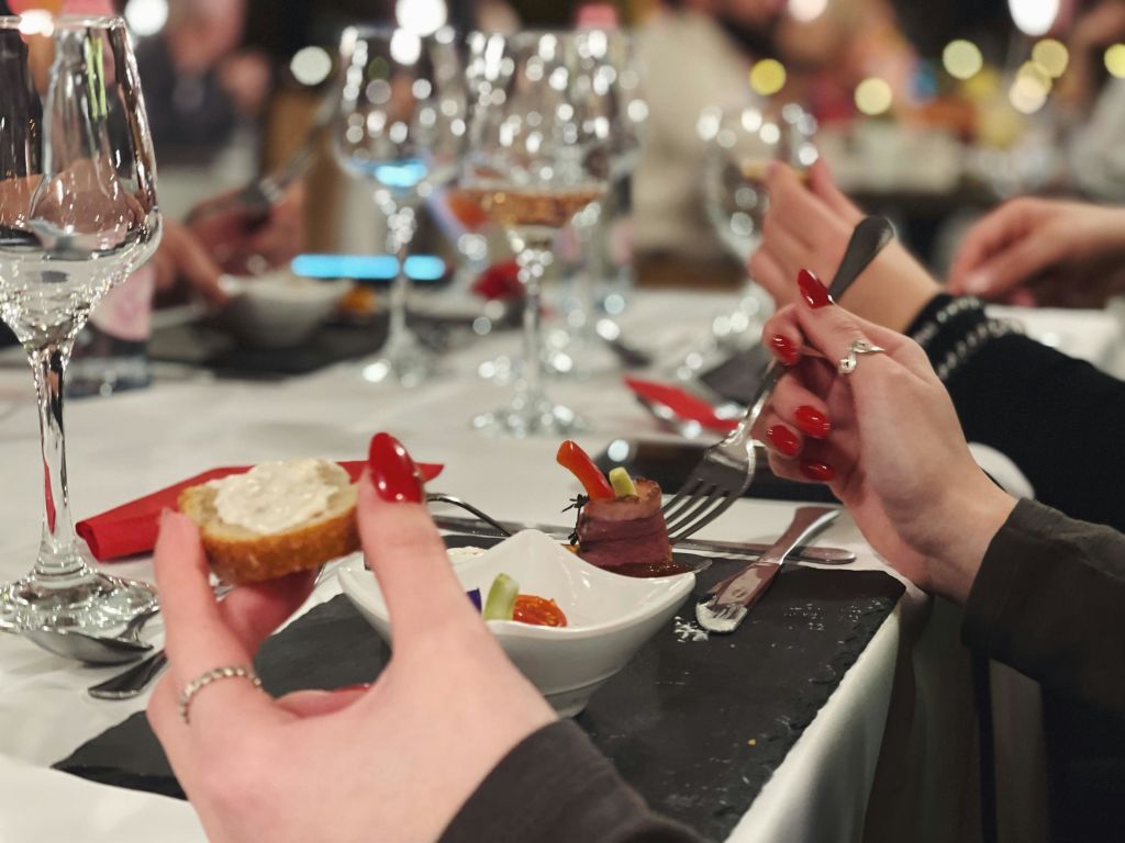 빵 조각과 포크를 들고 빨간 손톱을 든 손의 클로즈업, 와인잔과 작은 음식 접시가 놓인 테이블에서의 식사.