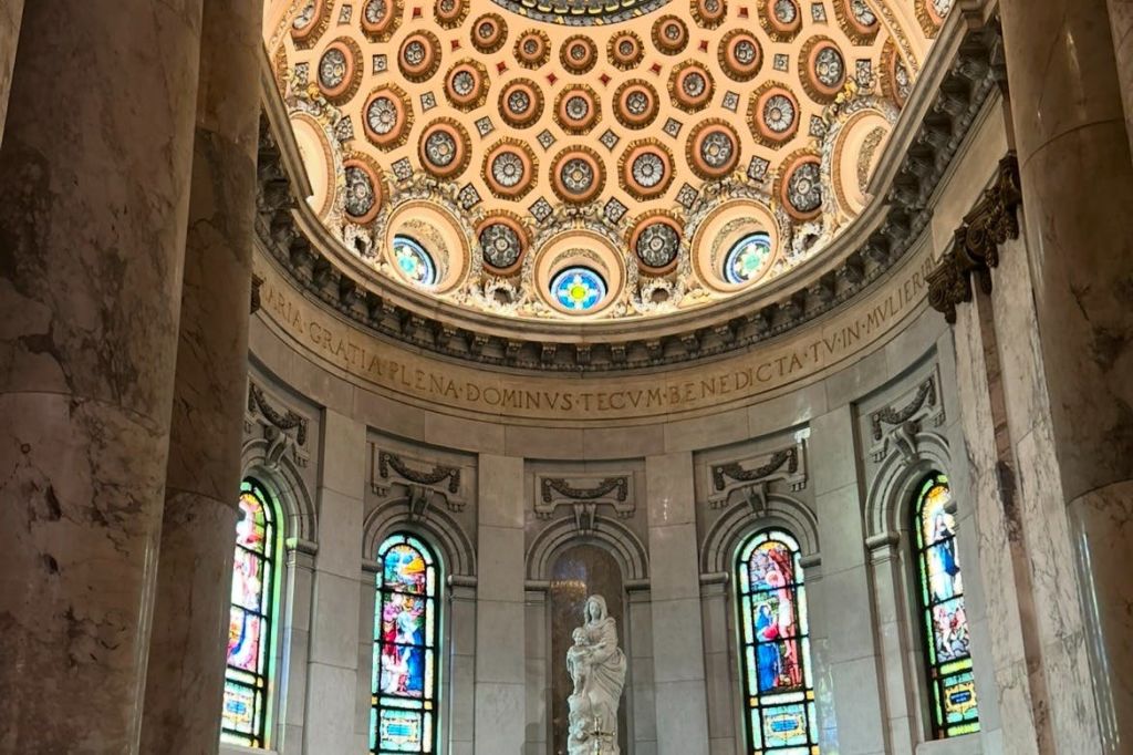 돔형 천장, 스테인드글라스 창문, 종교적 인물의 중앙 동상이 있는 화려하게 장식된 대성당 내부.