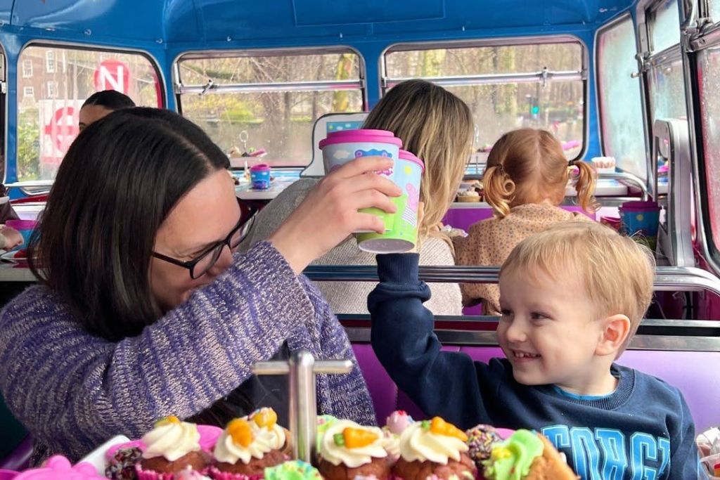 컵케이크와 다른 사람들이 배경으로 보이는 다채로운 버스 스타일의 분위기에서 웃으며 컵을 들어 올리는 아이.