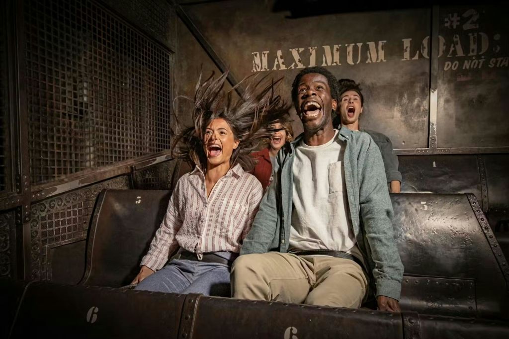 테마파크에 앉아 있는 네 명의 사람들이 흥분과 놀라움의 표정으로 머리카락을 뒤로 날려보냅니다.