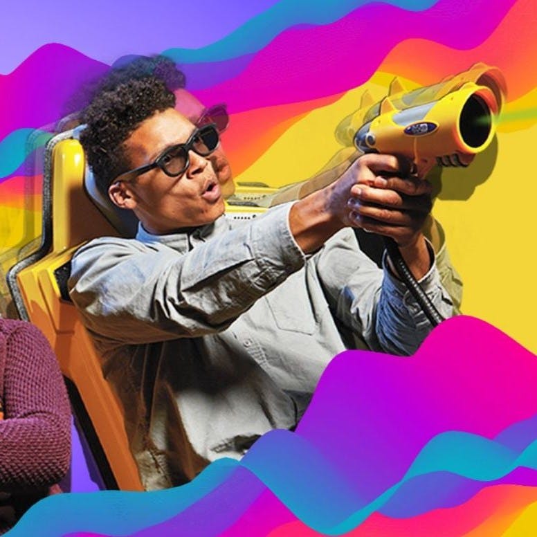 선글라스를 착용한 사람이 노란색 의자에 앉아 노란색 장난감 총을 들고 화려한 물결을 배경으로 앉아 있습니다.