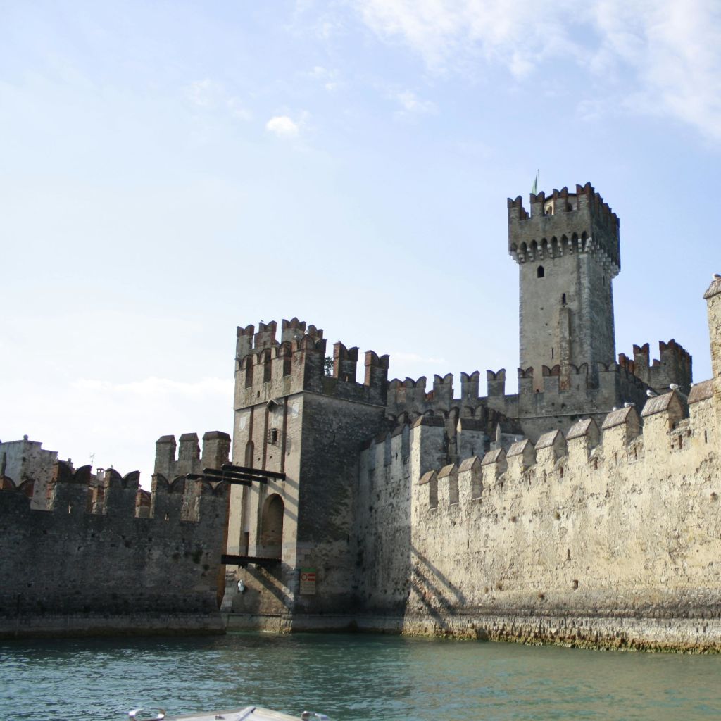 포탑과 전투가 있는 중세 석조 성은 부분적으로 흐린 하늘 아래 잔잔한 물줄기에 인접해 있습니다.