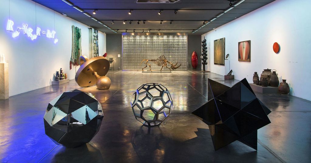 기하학적 조각, 코뿔소 해골, 벽에 걸린 다양한 예술 작품, 광택이 나는 콘크리트 바닥이 있는 현대 미술관입니다.
