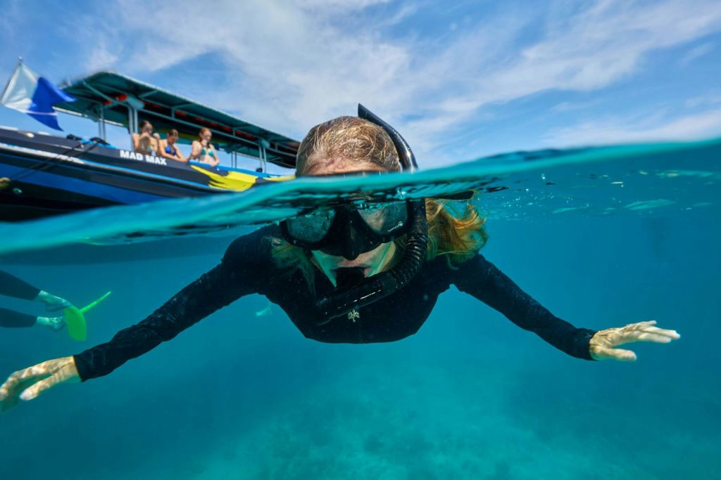 마스크와 스노클링을 착용한 스노클러가 보트 근처의 맑고 푸른 물에 떠 있습니다.