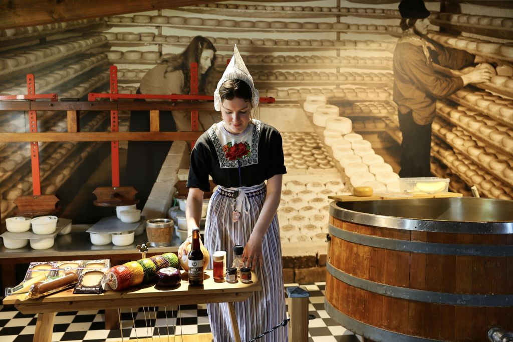 네덜란드 전통 복장을 한 여성이 치즈와 양념이 놓인 테이블 근처에 서 있습니다.