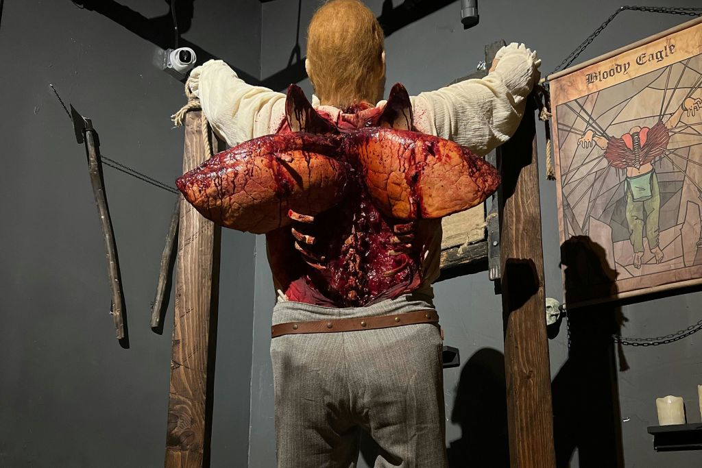 나무 액자와 소품이 놓인 조명이 희미한 방에 화사한 등 상처가 있는 마네킹이 전시되어 있습니다.